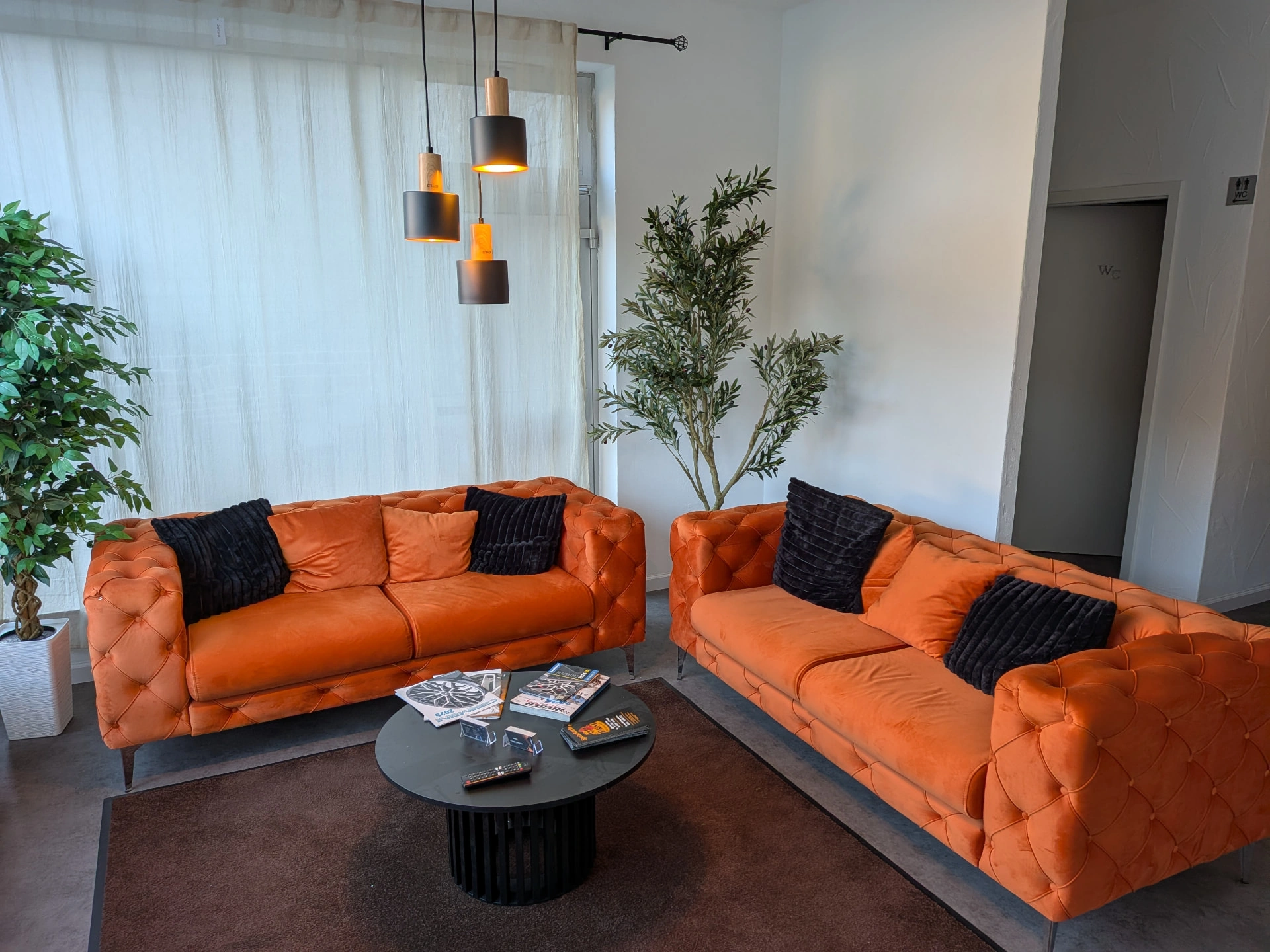Wartebereich mit orangen Sofas, Couchtisch und Prospekten bei W&S Automotive